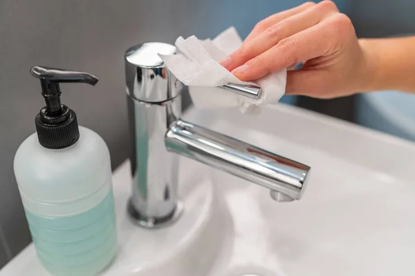 El hijyenik elleri, COVID-19 'un kirlenmesini önlemek için ellerini kuruttuktan sonra musluğu kağıt havluyla yıkıyor. Banyoyu temizliyorum. — Stok fotoğraf