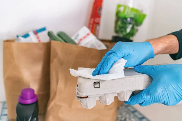 Cleaning groceries man at home wiping egg package with sanitizing wipes at home after shopping or receiving online delivery grocery store bags — Stock Photo, Image