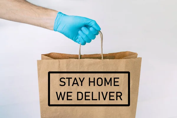 COVID-19のために手袋で届けられた宅配食品は、コロナウイルスの社会的距離から隔離されます。テキストメッセージ: STAY HOME, We Deliver man giving bag asコロナウイルス防止 — ストック写真