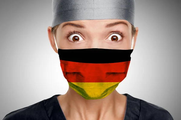 La doctora asiática sorprendió a la doctora alemana por la ayuda de la crisis COVID-19 con la bandera de Alemania en máscara quirúrgica. Trabajadores sanitarios que necesitan ayuda del PPE para luchar contra el Coronavirus COVID-19 — Foto de Stock