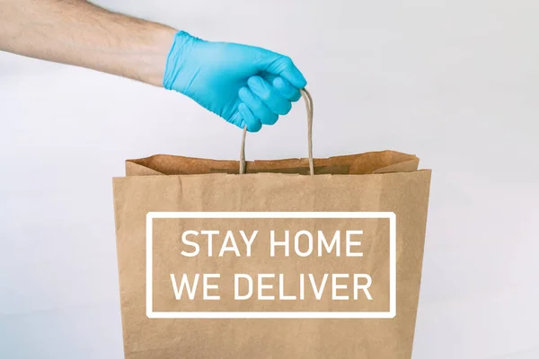 COVID-19のために手袋で届けられた宅配食品は、コロナウイルスの社会的距離から隔離されます。テキストメッセージ: STAY HOME, We Deliver man giving bag asコロナウイルス防止 — ストック写真