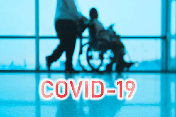 COVID-19 billboard red text on blue medical hospital background with doctor walking with disabled patient in wheelchair — Stock Photo, Image