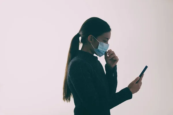 COVID-19 maskeli bir kadın yürürken ve cep telefonuna mesaj atarken yüzüne dokunuyor. — Stok fotoğraf