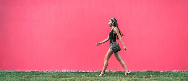 COVID-19 μάσκα φορούν στο κορίτσι της πόλης περπάτημα φορώντας μάσκα ως πρόληψη coronavirus έξω στην πόλη κατά δρόμο ροζ τοίχο πανό φόντο. Ιός Corona νέος τρόπος ζωής — Φωτογραφία Αρχείου