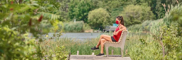 Máscara vestindo mulher sentada relaxando no banco do lado de fora no parque natural de verão para prevenção de coronavírus. Cara protectora cobrindo o estilo de vida COVID-19. Banner panorâmico — Fotografia de Stock