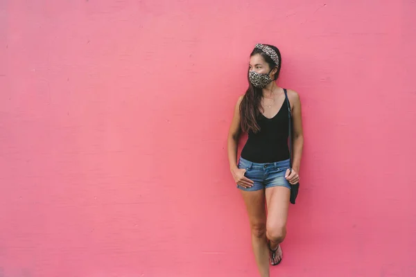 Mujer asiática apoyada en la pared rosa con máscara facial de tela en estampado de patrón de leopardo de moda. Los jóvenes casuales estilo de vida de la ciudad durante el virus corona — Foto de Stock