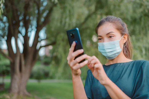 얼굴 마스크를 쓰고 코로나 바이러스가 유행하는 동안 밖을 걷는 동안 휴대 전화 추적 앱을 사용하는 여성. 도시 생활 — 스톡 사진