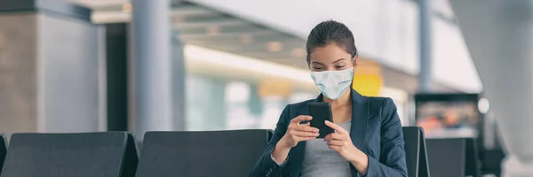 얼굴에는 마스크를 착용하여 입을 가리고 있다. Asian woman using mobile phone app waiting flight off in airport terminal banner. 아시아 여성, 공항 터미널에서 대기중. 코로나 바이러스가 유행하는 동안 파노라마처럼 퍼지는 여행 관광객들 — 스톡 사진