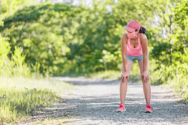 Dýchající unavená aktivní běžkyně s obličejovou maskou pro COVID-19 při běžeckém cvičení vyčerpaná s přestávkou v letním vedru venkovní běh stezky. Ochrana proti koronaviru — Stock fotografie