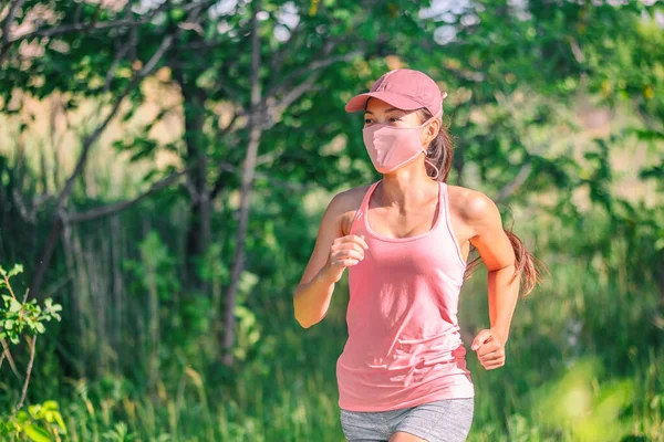 COVID-19 koruma tatbikatı sırasında maske takan Asyalı kız yaz parkı doğasında koşu sporu yaparken yüzünü kapatarak koşuyor. Pembe maske, şapka, kolsuz bluz. — Stok fotoğraf