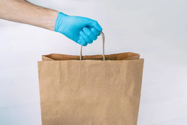 Home delivery during COVID-19 quarantine from coronavirus self isolation lockdown. Grocery store shopping delivery man giving paper bag wearing blue glove as protection for Corona virus prevention — Stock Photo, Image
