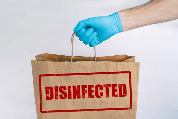 Delivery bag to home from online grocery shopping with stamp of safety DISIFINFECTED written on the paper side. Man holding groceries with medical blue glove — Stock Photo, Image