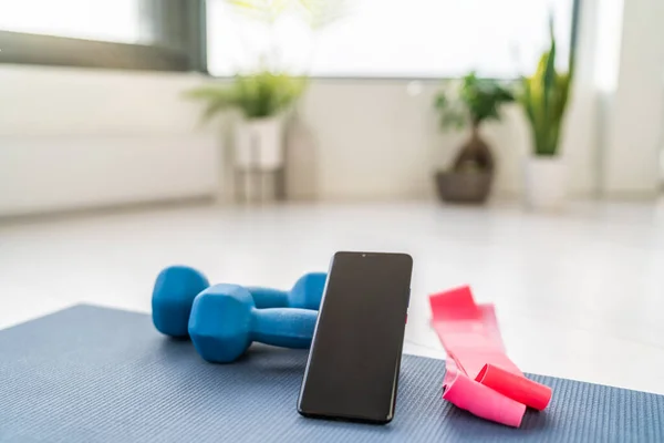 Gimnasio en casa ejercicios de entrenamiento en línea en la aplicación de teléfonos inteligentes para el entrenamiento en interiores en el apartamento con pesas pesas y bandas de resistencia en la sala de estar —  Fotos de Stock