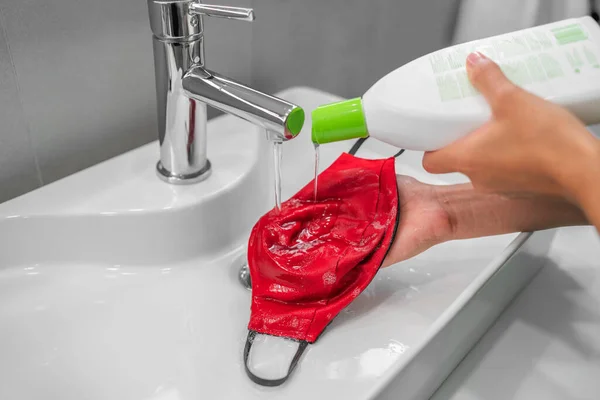 Washing face mask at home sink with liquid laundry soap by hand. Cloth reusable masks need to be cleaned