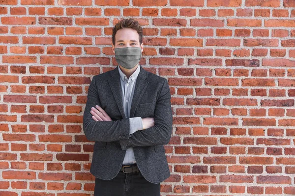 사업가는 코로나 바이러스 예방을 위해 얼굴 마스크를 쓴 초상화를 도시의 벽돌 배경에 걸고 있다. 교차 된 무기 사업가 혹은 부동산 중개업자 — 스톡 사진