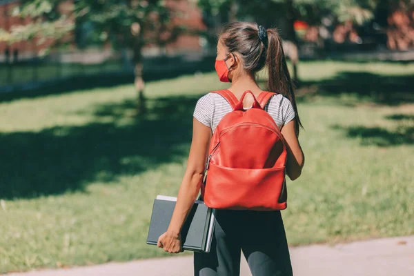 Μάσκα υποχρεωτική στην πανεπιστημιούπολη για πίσω στο σχολείο φοιτητής κορίτσι φορώντας προστατευτικό πρόσωπο που καλύπτει το περπάτημα με βιβλία και σακίδιο. Κολεγιακή νεαρή γυναίκα — Φωτογραφία Αρχείου