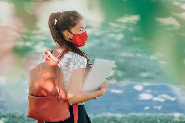 Terug naar school universiteitsstudent Aziatische vrouw met gezichtsmasker op de campus lopend met rode rugzak, boeken en laptop. Coronavirus realiteit — Stockfoto