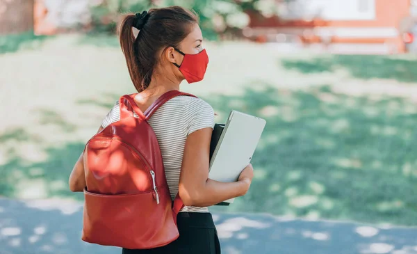 Ritorno a scuola studentessa universitaria indossando maschera civettuola passeggiando nel campus con zaino, libri e laptop. Stile di vita del virus Corona — Foto Stock