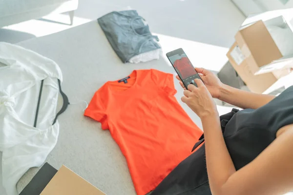 Online verkopen via telefoon app het nemen van mobiele foto van t-shirt doen e-commerce kleine bedrijven thuis — Stockfoto