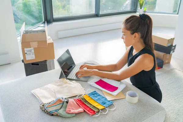 Онлайн малый бизнес предприниматель женщина работает удаленно из дома на ноутбуке продажи ткани маска ручной работы из ткани на приложение электронной коммерции для COVID-19 — стоковое фото