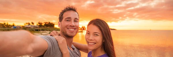 Mutlu selfie çiftleri panorama tatili ilanı Florida sahilinde gün batımında fotoğraf çekiyor. Gülümseyen Asyalı kadın ve Kafkasyalı erkek, ırklar arası ilişki — Stok fotoğraf