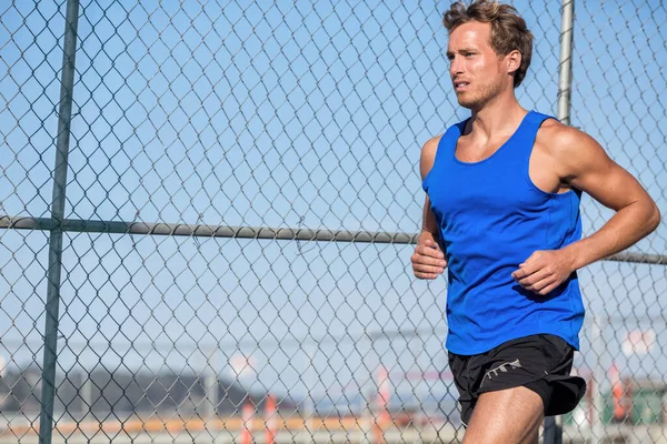 Friska idrottare löpare man - urban stad livsstil. Unga sport hane kör i grunge staket bakgrund utomhus på sommaren bär blå tank top. Aktivt boende. — Stockfoto