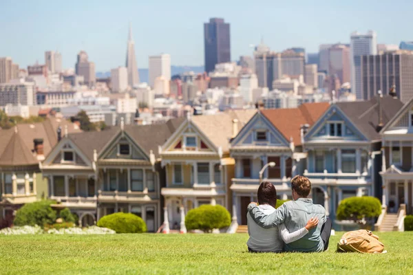 Atração turística de São Francisco na Alamo Square, a famosa fila de postais Painted Ladies, viagem à Califórnia. Casal turistas relaxando na grama desfrutando de destino popular. Estilo de vida das pessoas — Fotografia de Stock