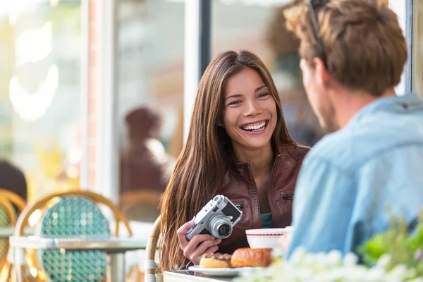 Un par en la cafetería estilo de vida. Jóvenes turistas desayunando en la mesa del restaurante en la terraza de la acera en el bistró parisino en la ciudad europea. Mujer asiática viajero con cámara vintage. Europa turismo. — Foto de Stock