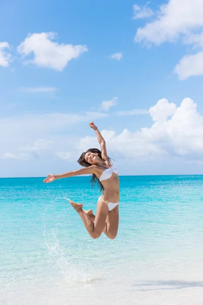 Leuke bikini vrouw springen op het strand spetterend water — Stockfoto