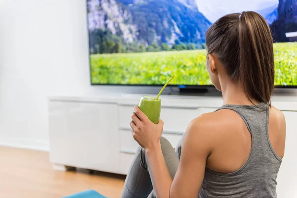 Casa mujer bebiendo batido verde viendo la televisión —  Fotos de Stock