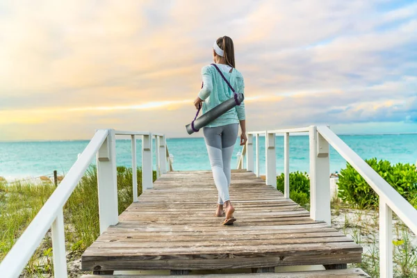 Mujer fitness caminando con esterilla de yoga en la playa — Foto de Stock