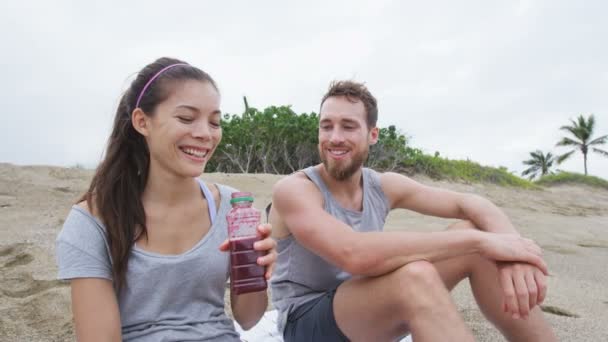 Pareja compartiendo jugo de remolacha en la playa después del ejercicio — Vídeos de Stock