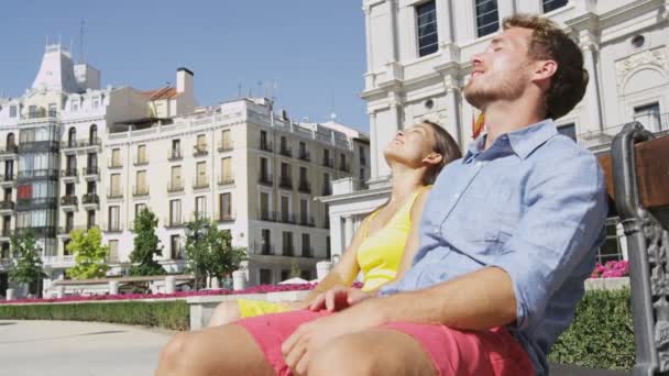 Ζευγάρι χαλαρώνοντας στον πάγκο απολαμβάνοντας τον ήλιο με τα μάτια κλειστά στην πλατεία της πόλης στη Μαδρίτη — Αρχείο Βίντεο