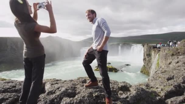 Pareja tomando fotos con teléfono inteligente divirtiéndose por la cascada Godafoss en Islandia — Vídeo de stock