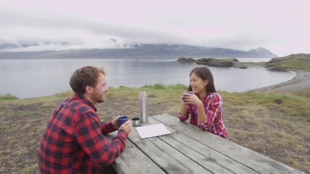 Пара кемпингов, сидящая за столом и пьющая кофе на озере — стоковое видео