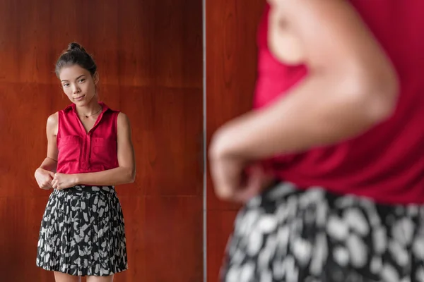 Yeni kıyafetler deneyen bir kadın soyunma odasında aynaya bakıyor elbise mağazasında etek alışverişi yapıyor. Mutlu Asyalı kız görünüşünden memnun, kilo verme konsepti — Stok fotoğraf