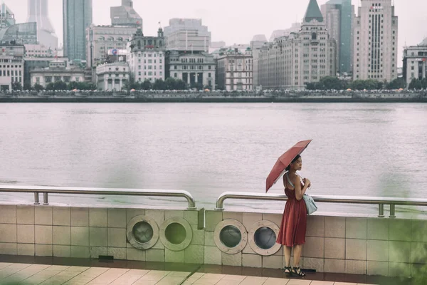 Shanghai stad bund flod asiatisk kvinna promenader under regn med paraply på Kina Asien semester. Elegant kinesisk turist dam i röd klänning — Stockfoto