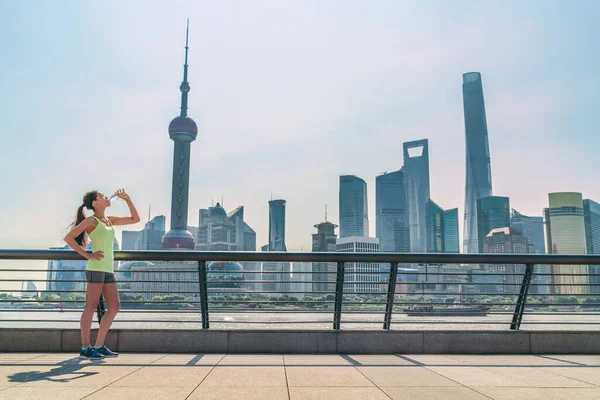 Shanghai skyline fitness femme assoiffée bouteille d'eau potable le jour ensoleillé, en Chine. Asiatique jogger soif boisson étanche — Photo