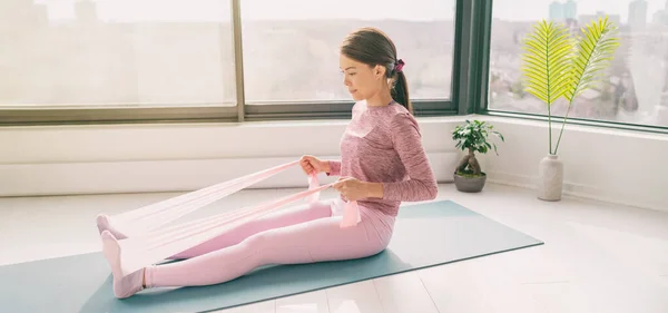 Αντίσταση μπάντα σπίτι προπόνηση φυσικής κατάστασης γυναίκα προπόνηση με κωπηλασία βραχίονα άσκηση χρησιμοποιώντας λαστιχάκια για yoga mat ασκήσεις δαπέδου με ελαστικό ιμάντα. Πανοραμική σημαία — Φωτογραφία Αρχείου