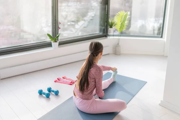 Vrouw die thuis traint benen te strekken voor yoga training training. Fitness thuis meisje uit te werken in de ochtend zonlicht in de woonkamer van appartement — Stockfoto