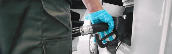 气泵科罗纳威病毒爆发防护手套，用于在加油站横幅全景泵送汽油时触摸手柄。COVID-19大流行病期间原油价格下跌 — 图库照片