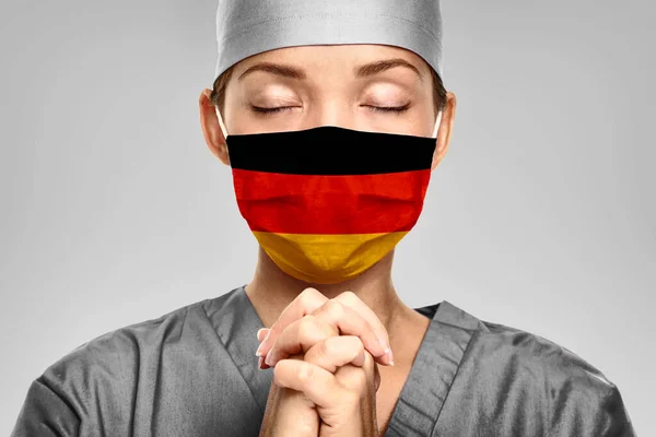 German doctor praying for help with Germany flag on surgical mask. Young woman medical needing PPE help to fight COVID-19 Coronavirus — Stock Photo, Image