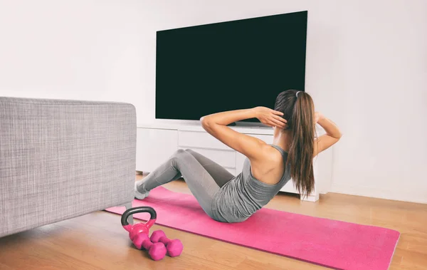 Hem Fitness kvinna gör styrketräning abs situps kroppsvikt golv övningar titta på online livestream träning webb videor gjutna på smart tv i vardagsrummet i hus eller lägenhet — Stockfoto