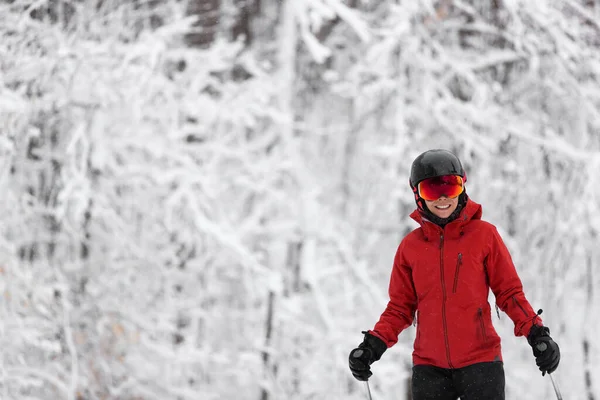 Sport invernali felice sciatore Sci alpino andando dowhill contro gli alberi innevati sfondo durante la tempesta di neve invernale. Donna in giacca rossa e occhiali — Foto Stock