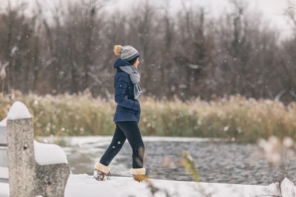 Inverno tempestade de neve feliz tempo frio menina andando em nevar floresta bosques fundo pelo lago em casaco acolhedor — Fotografia de Stock