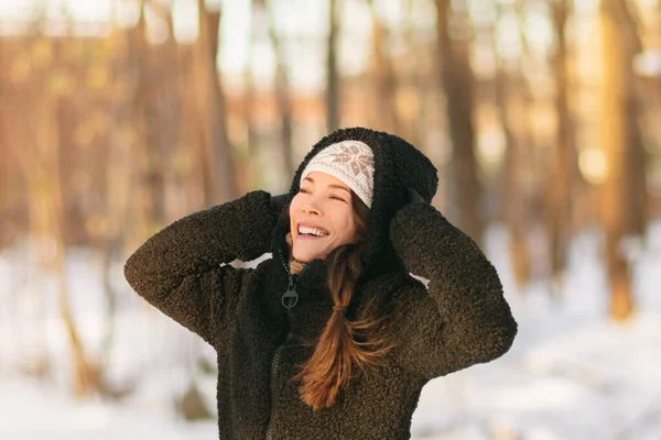 Diversión de nieve de invierno chica feliz caminando fuera en clima frío protegiendo las orejas sosteniendo sombrero de lana sobre las orejas estilo de vida activo al aire libre. Chica asiática con chaqueta de abrigo negro, guantes respirando aire fresco —  Fotos de Stock