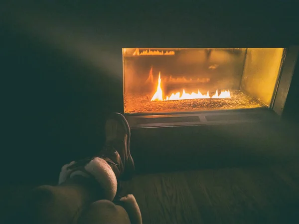 После горнолыжного курорта женщина в зимних сапогах сидит у газового биоэтанола камина ночью уютное камин с пламенем светящимся в темноте — стоковое фото
