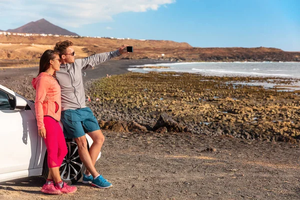 Road trip pár turistů brát selfie na okružní přestávce příroda pláž krajina na cestách dovolenou na Kanárských ostrovech. Žena a muž přátelé řízení aut v Lanzarote, Evropa — Stock fotografie