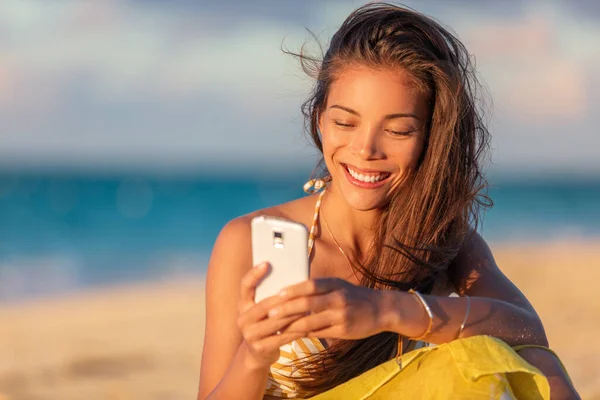 Mutlu Asyalı genç bir kadın sahilde tatilde internetten cep telefonuyla mesajlaşıyor yaz tatili yaşam tarzı, tatilde rahatlayan çok ırklı Çinli kız turist. — Stok fotoğraf