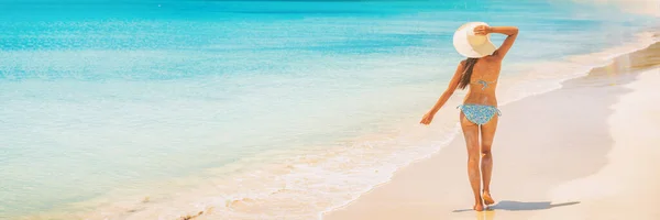 Beach Travel Férias de férias Mulher relaxante andando sobre idílica praia caribenha panorama banner fundo. Vista traseira do turista feminino em chapéu de sol e biquíni nas férias de verão. Férias despreocupadas — Fotografia de Stock